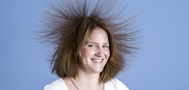 Frau mit vollem, struppigem Haar lächelt vor einem blauen Hintergrund.