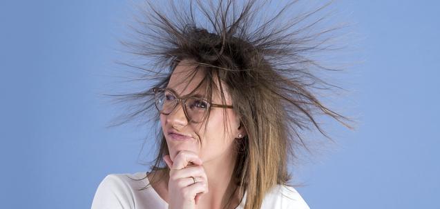 Frau mit zerzaustem Haar, trägt Brille und denkt nach, vor blauem Hintergrund.