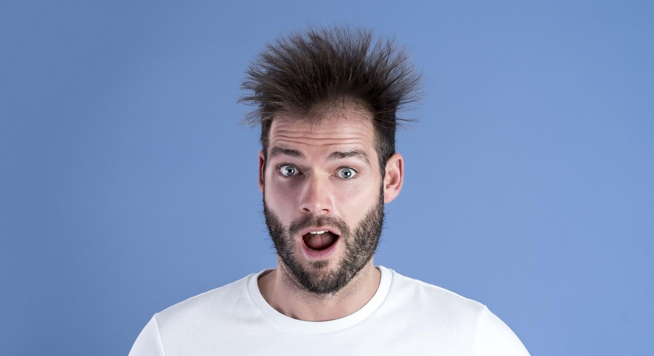 Mann mit zerzausten Haaren schaut überrascht und mit offenem Mund in die Kamera, Hintergrund in einheitlichem Blau.