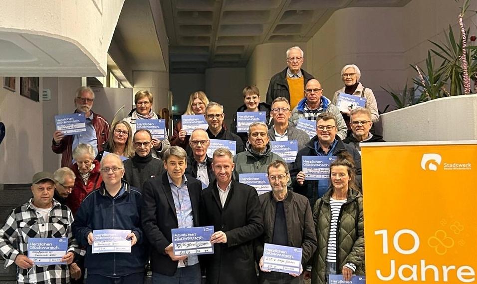 Gruppe von Personen, die Glückwunschschilder in der Hand halten, stehen zusammen in einem Innenraum.